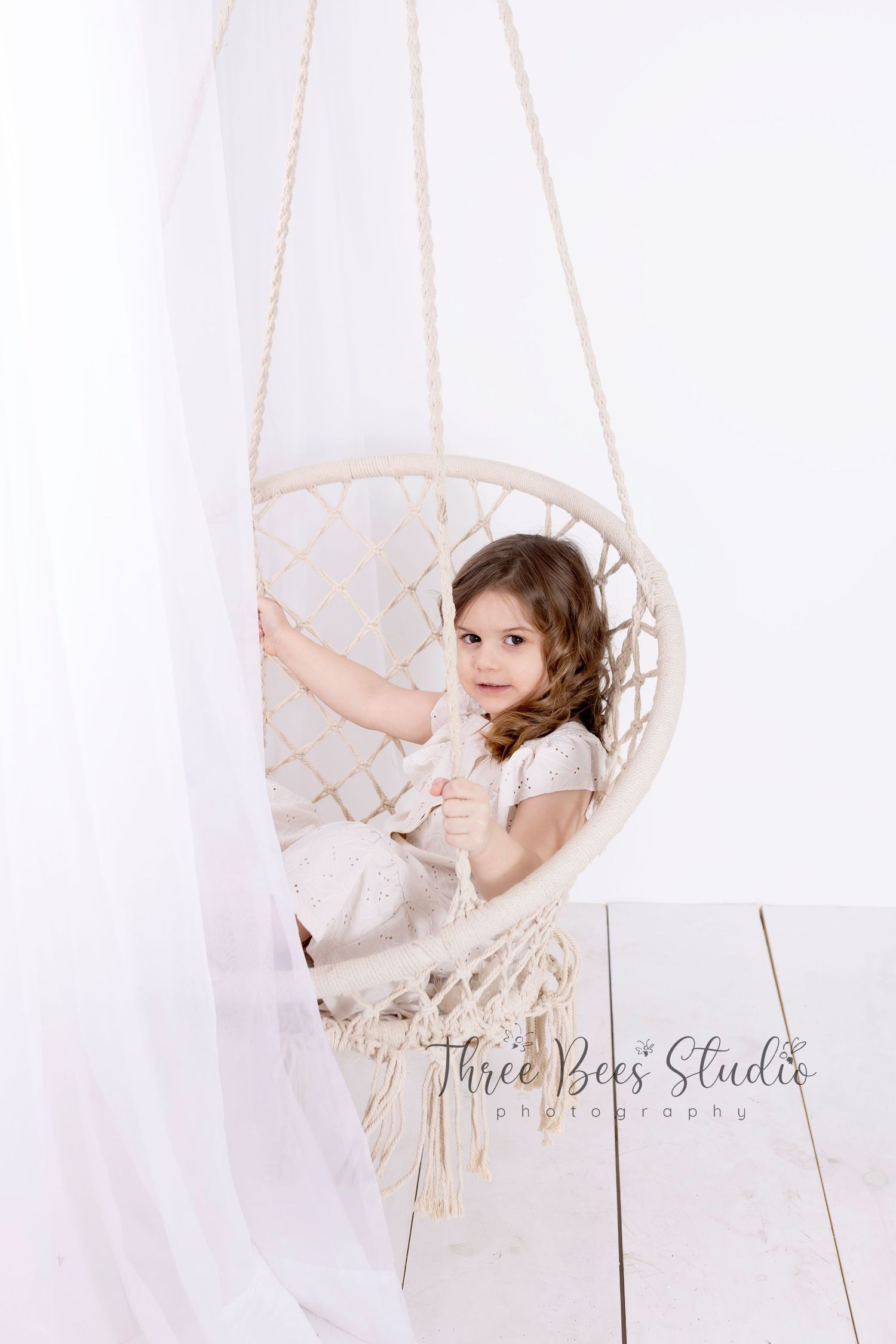A hanging macrame swing chair in white against a light backdrop with soft, dreamy lighting.