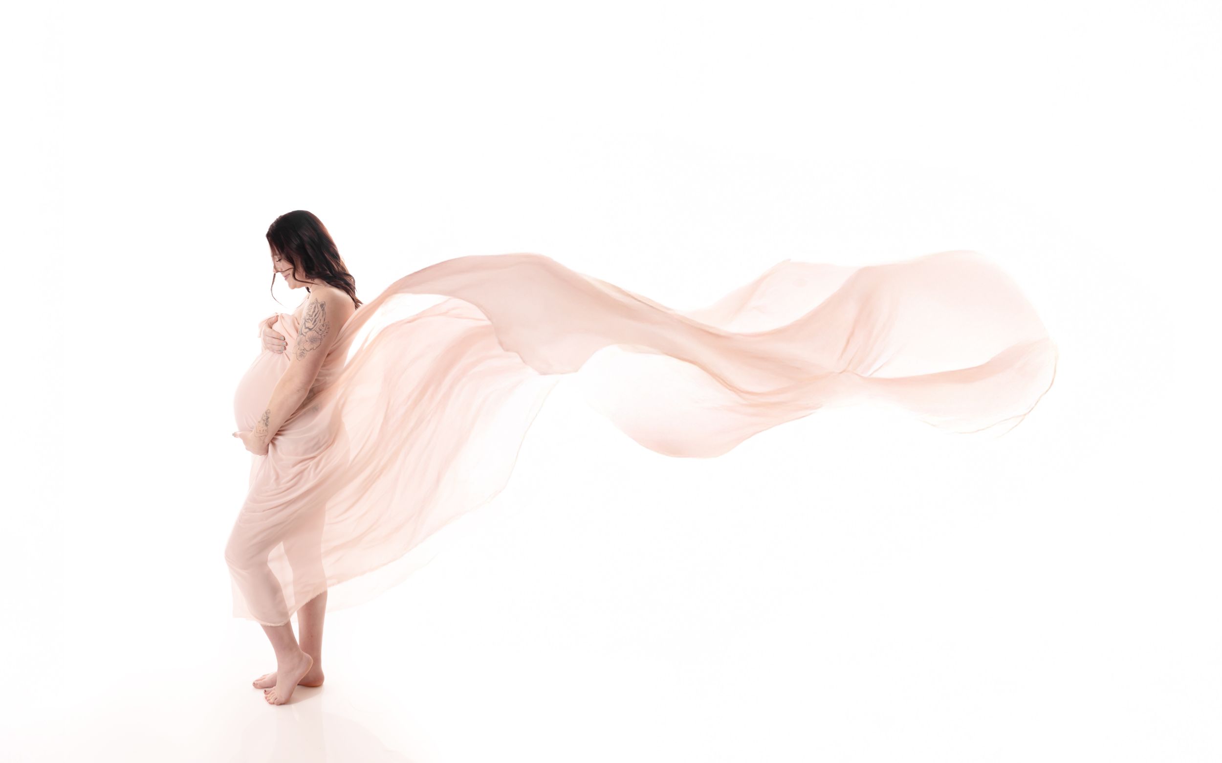 A graceful figure draped in flowing pink fabric poses against a white background creating an ethereal artistic effect.