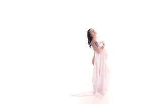 A person wearing a flowing white gown poses gracefully against a bright white background.
