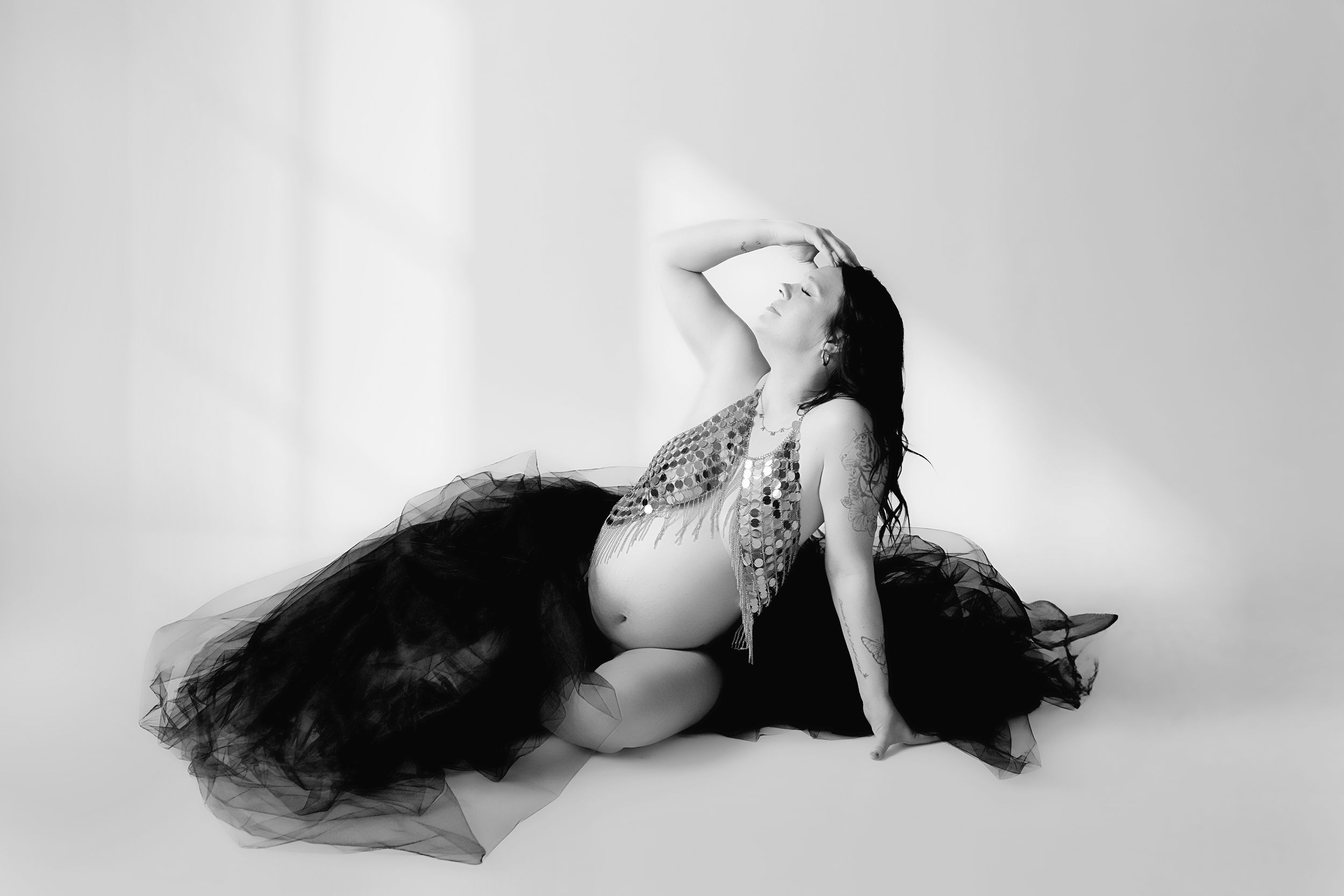 A person in black tulle skirt poses gracefully in a dramatic black and white maternity photo.
