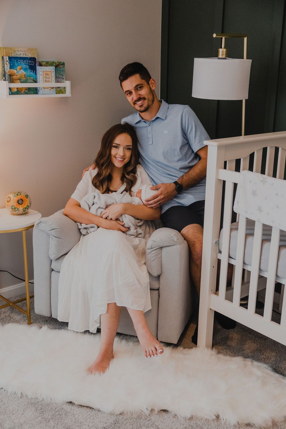 A couple sits together in a nursery room with white decor and a crib.