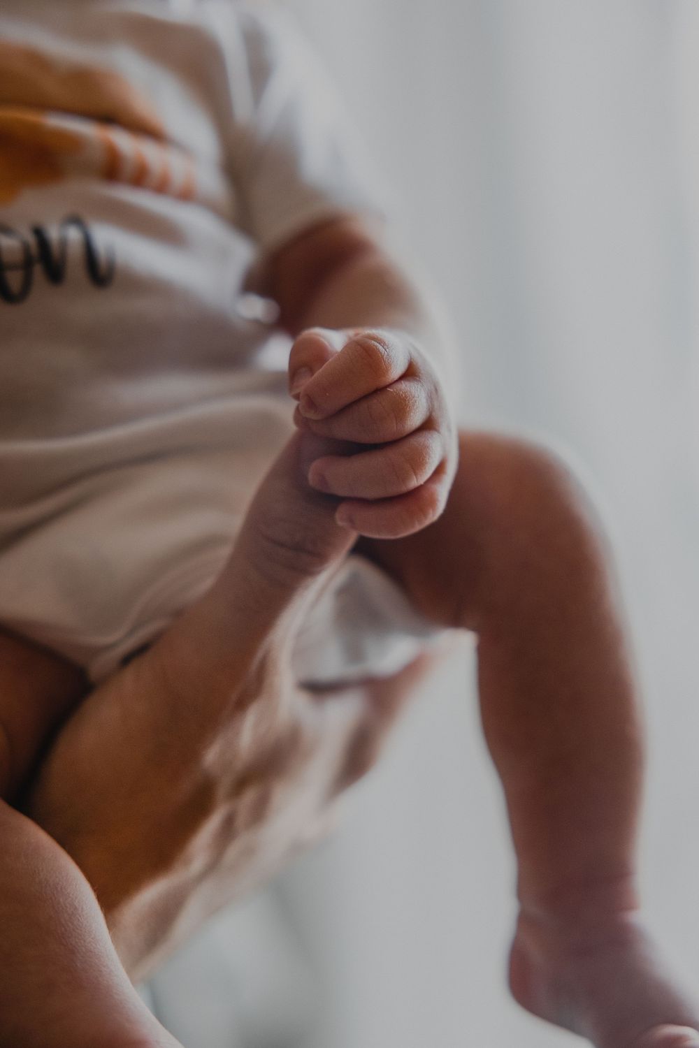 Close-up shot of baby's tiny hand grasping parent's finger.