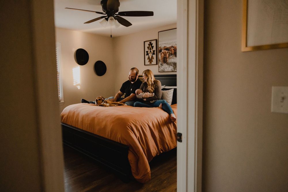 Family relaxing together on orange bedspread viewed through bedroom doorway.
