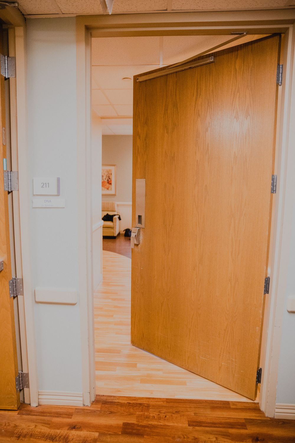 Open wooden hospital room door showing bright interior hallway.