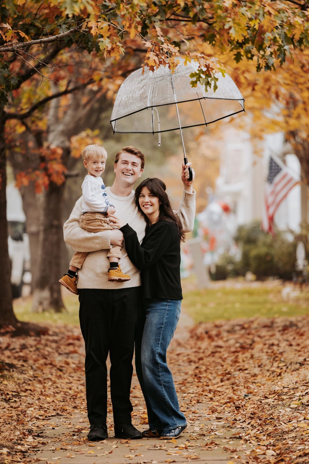 Family standing together under clear umbrella surrounded by fall leaves.