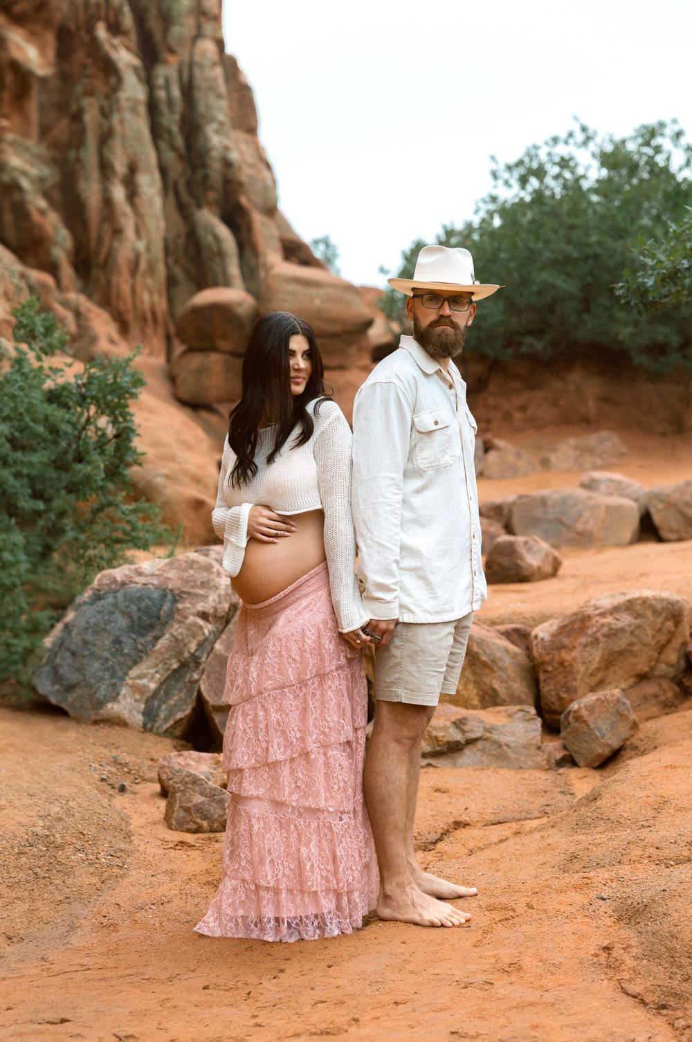 A romantic couples maternity photo session on a red rock trail with desert scenery in the background.
