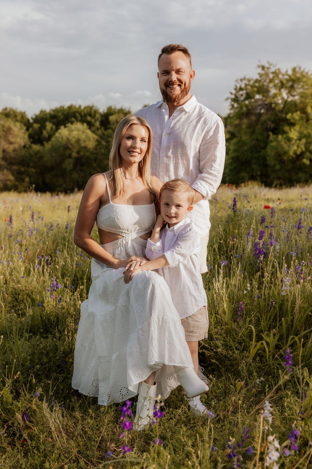 A family stands together in a wildflower meadow at sunset wearing white outfits.