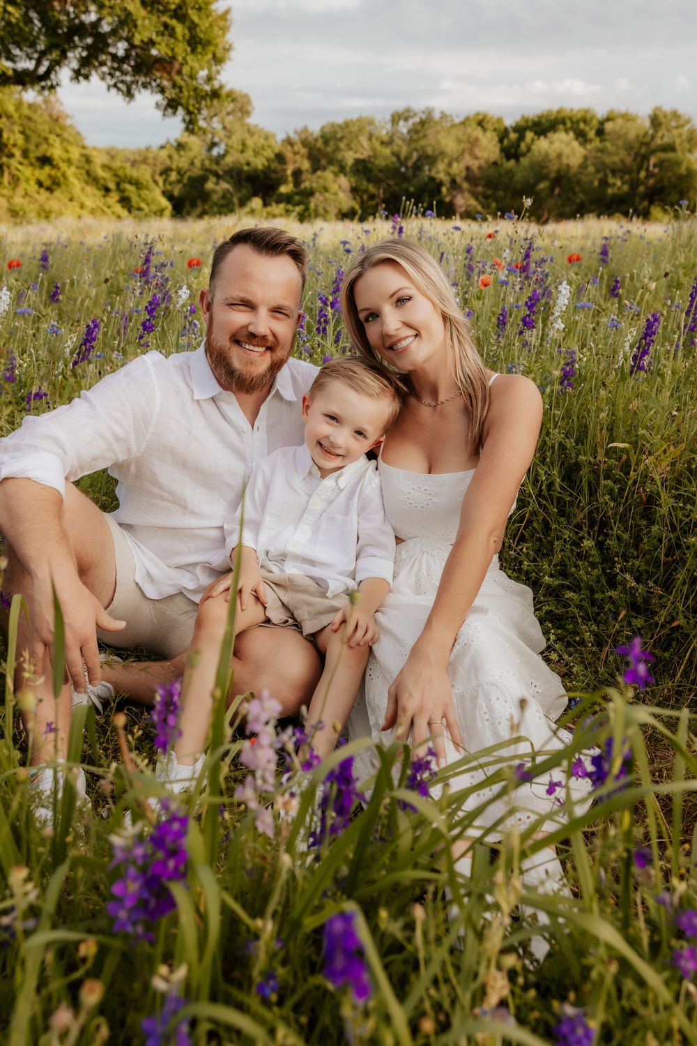 A family sits together in a field of purple wildflowers during a warm summer evening photoshoot.