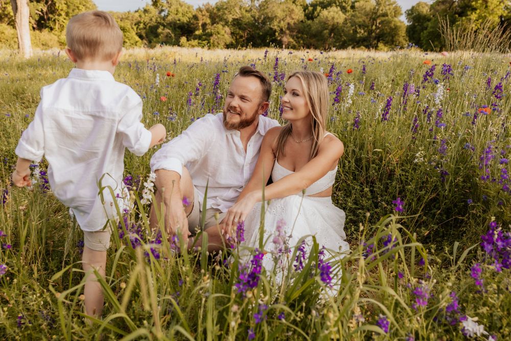 A couple sits together in a wildflower meadow filled with purple lupines on a warm summer evening.