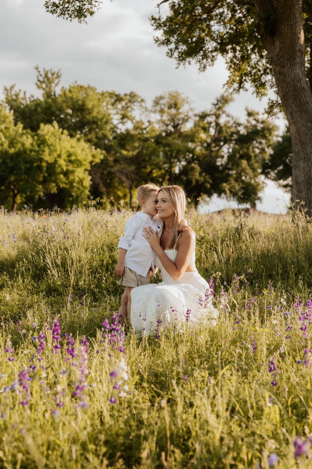 A tender moment captured in a sunlit meadow with wildflowers and tall grass during golden hour.