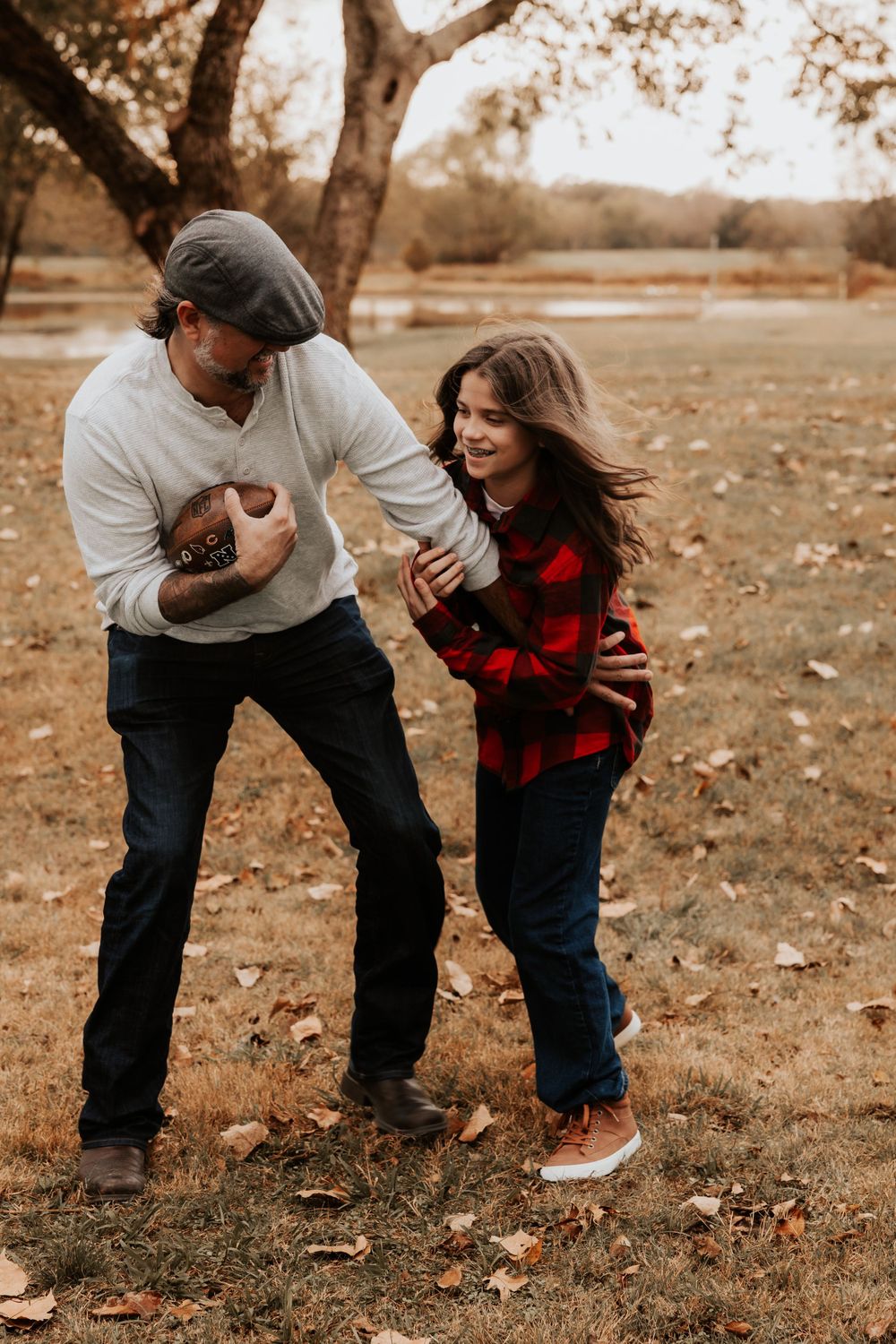 Two people in casual fall attire playing and laughing together on fallen leaves in a park during autumn.