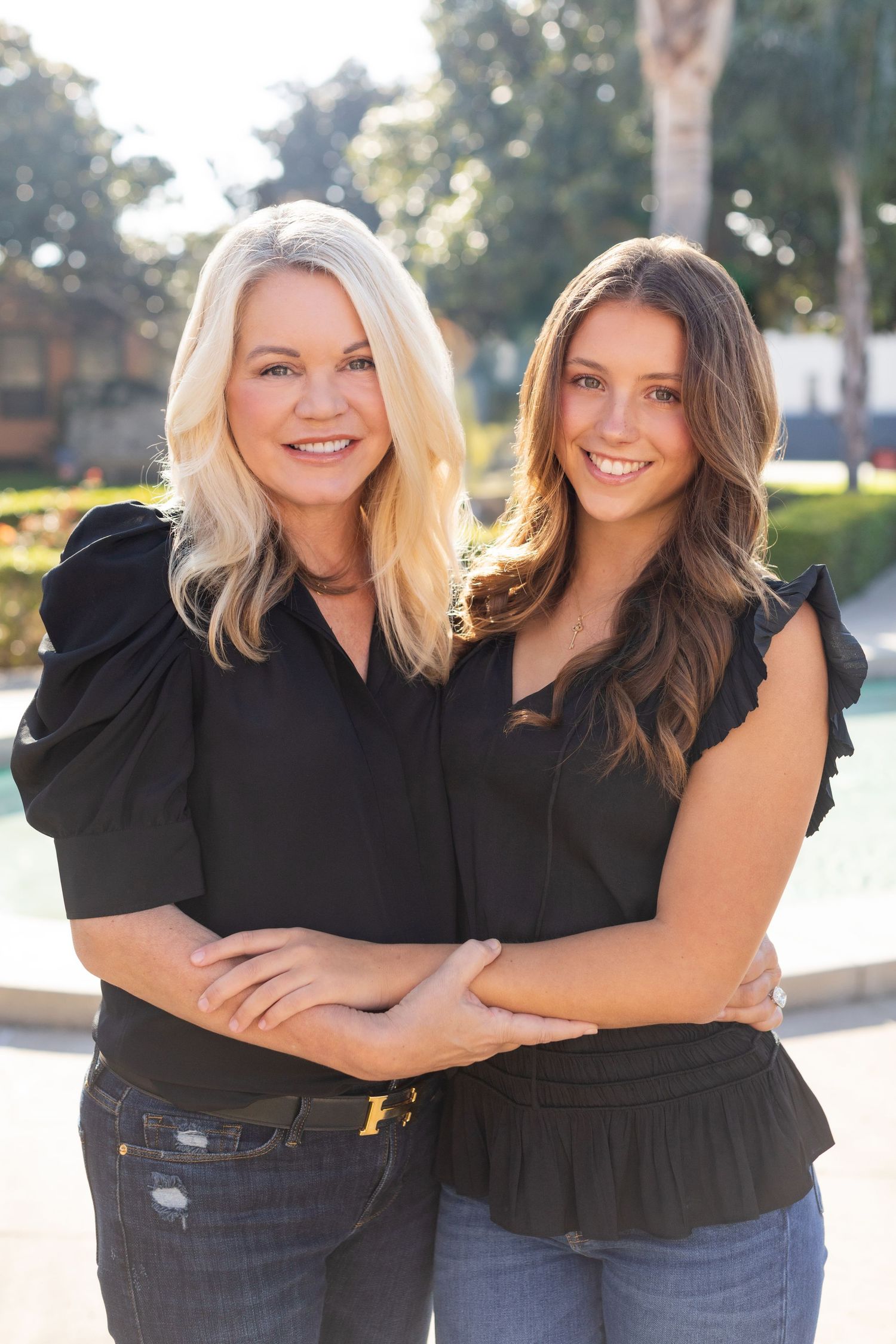 Two people wearing black tops pose close together against a blurred background.