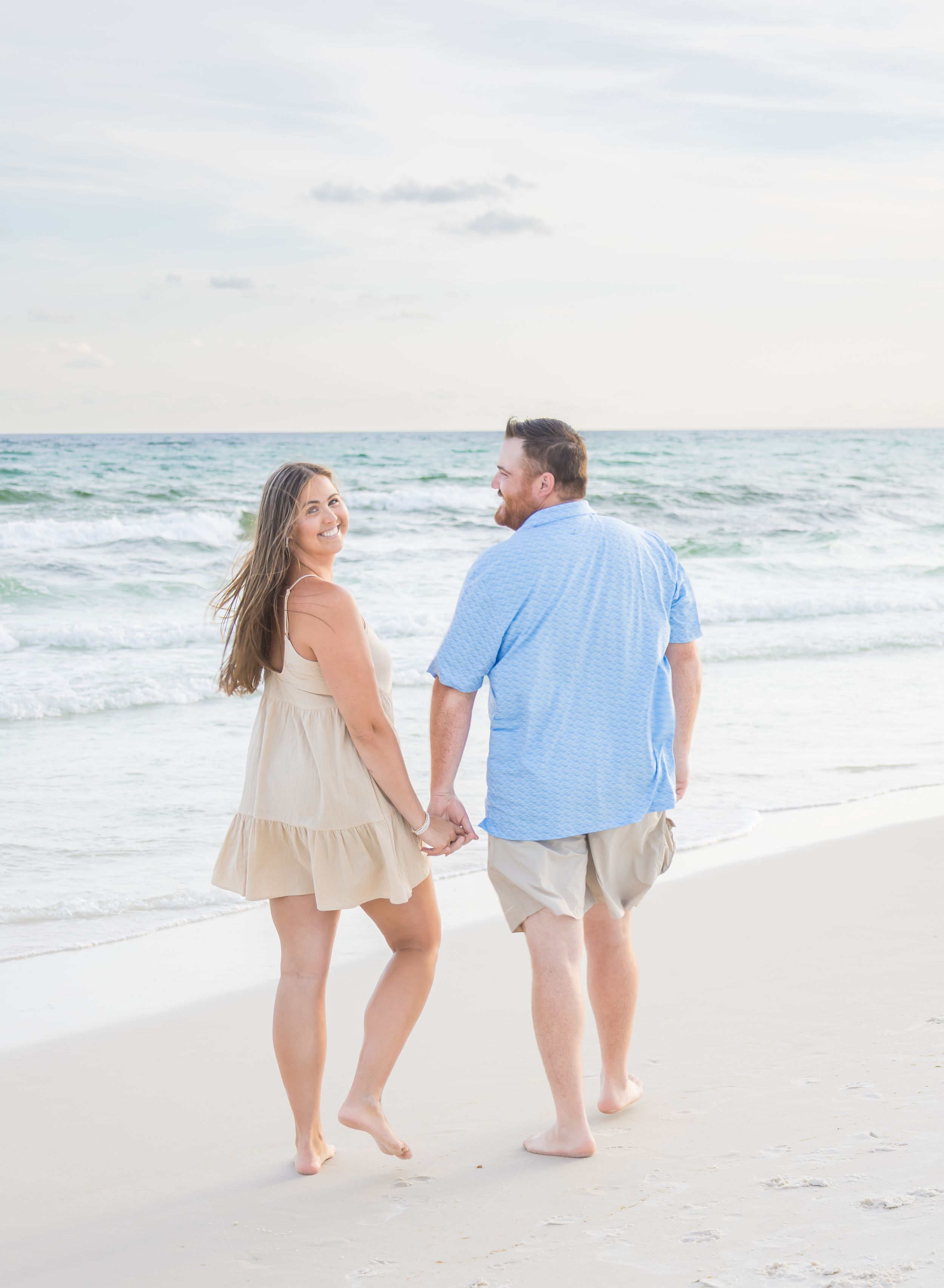 A couple strolls hand in hand along a serene white sandy beach with gentle waves rolling in from the ocean.