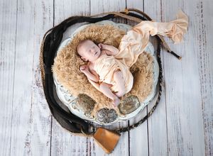 Newborn baby sleeping peacefully in a rustic bowl with fur lining and vintage western props.