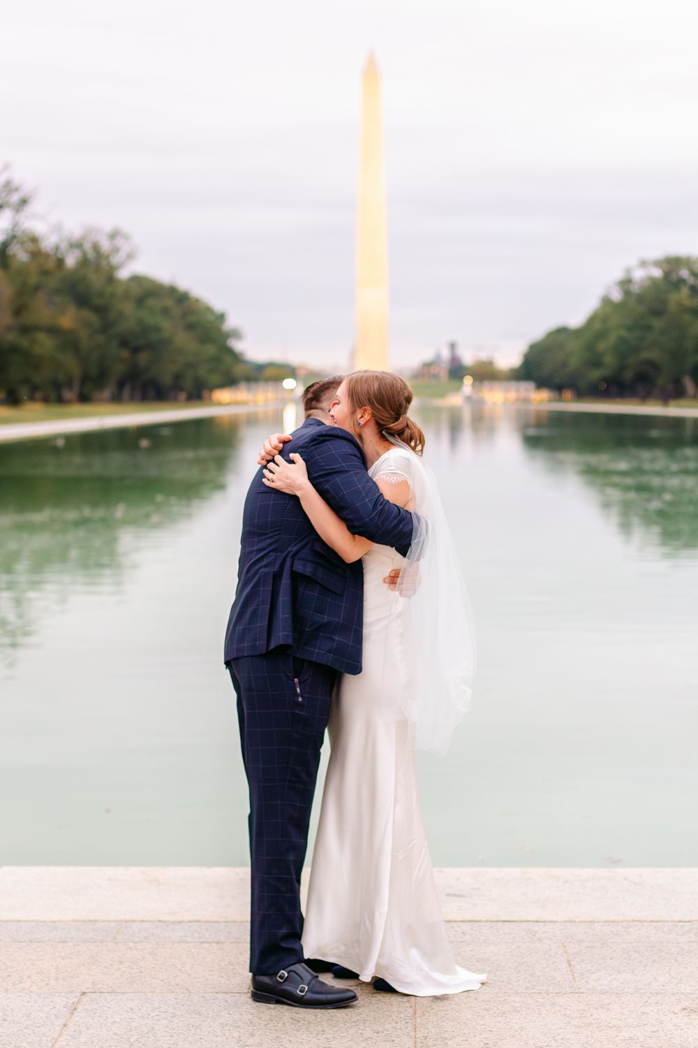 Bride and groom share a romantic kiss by the Reflecting Pool with Washington Monument behind them.