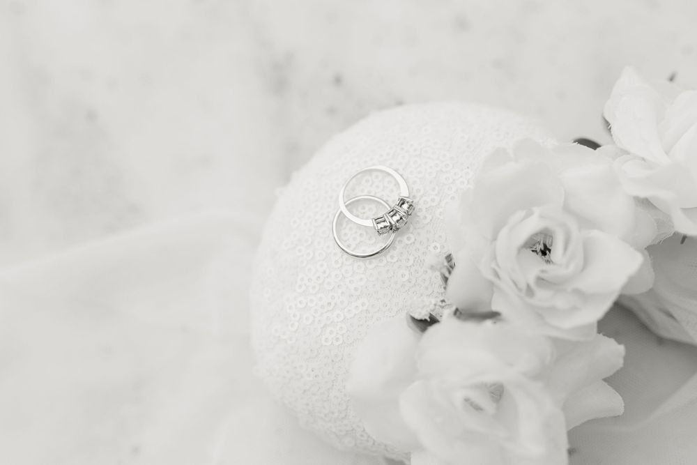 Wedding rings resting on a white pillow with delicate white roses and veil.