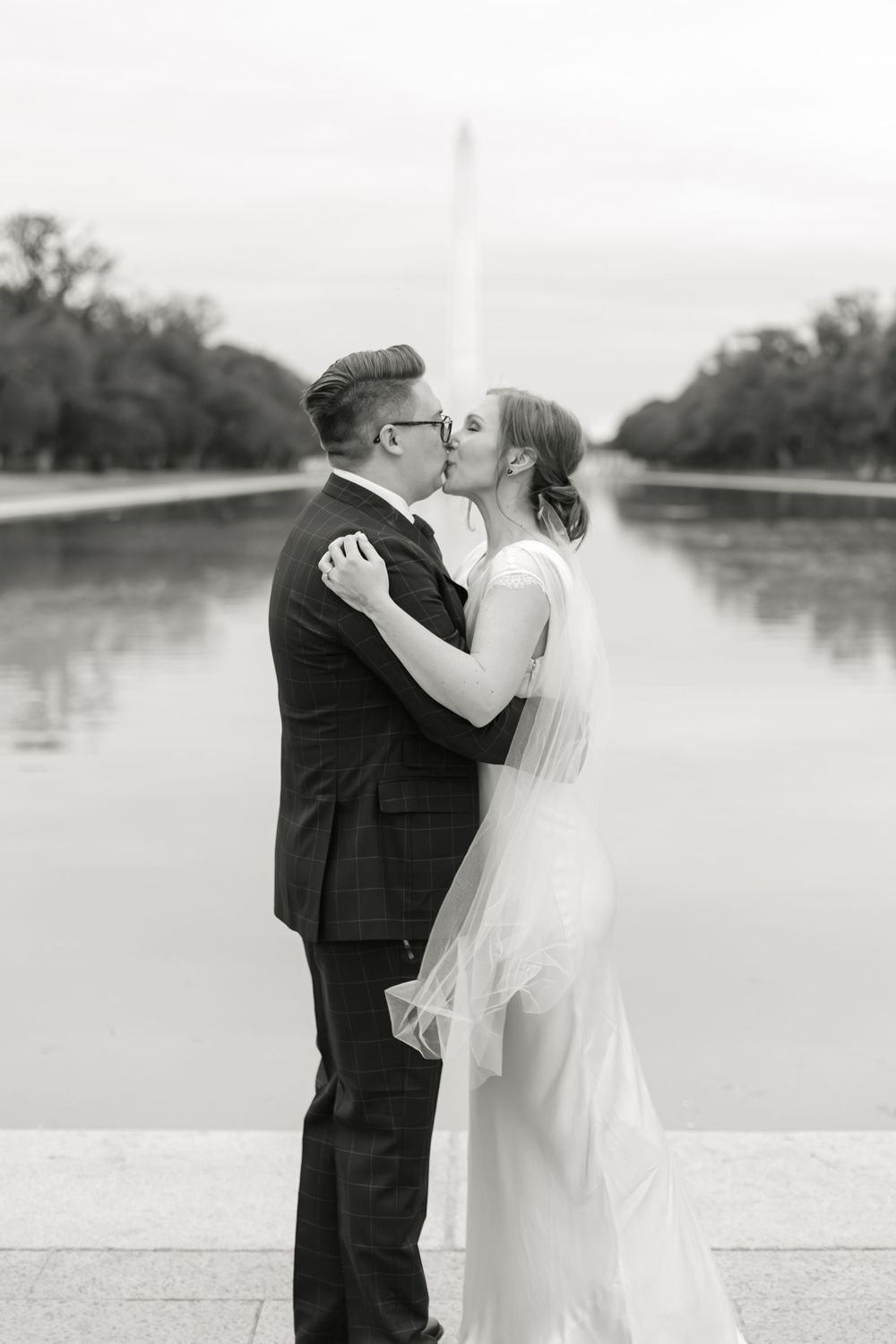 Black and white photo of bride and groom kissing at the Lincoln Memorial Reflecting Pool.