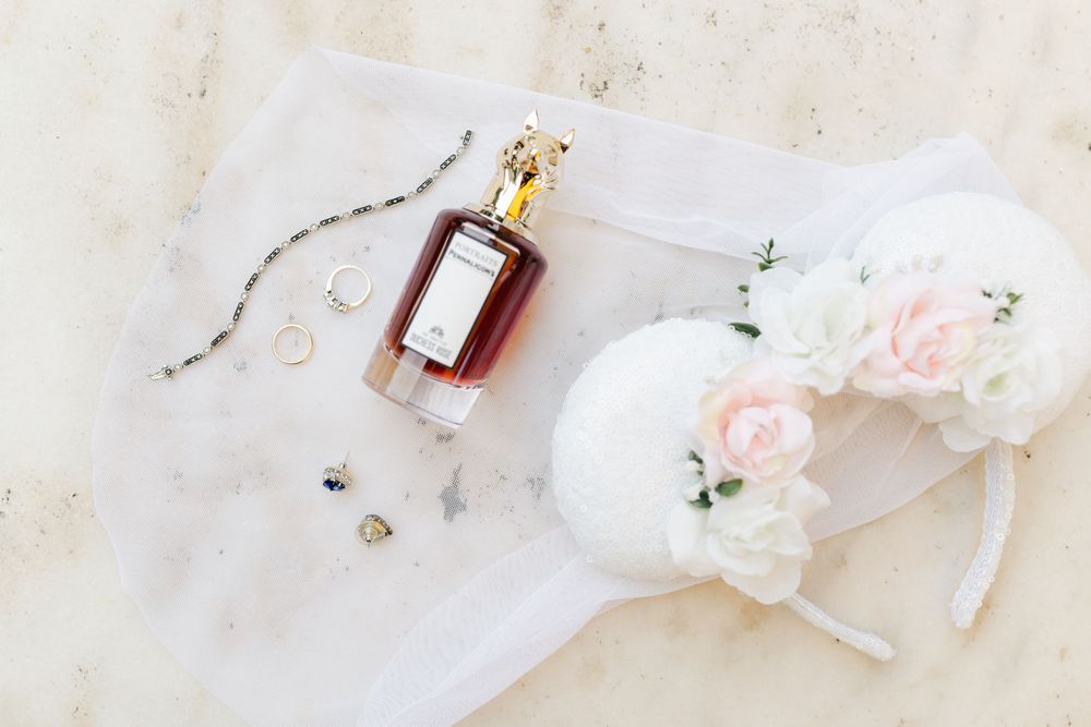Bridal flat lay with perfume bottle, wedding rings, veil, and floral headpiece.