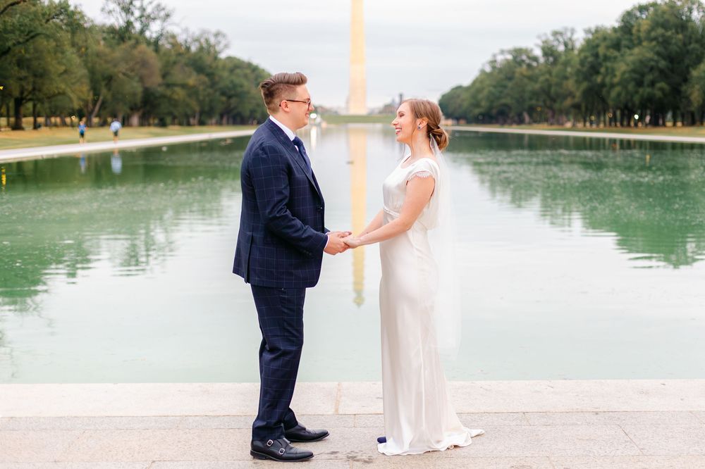 Bride and groom hold hands facing each other at the Reflecting Pool with Washington Monument view.