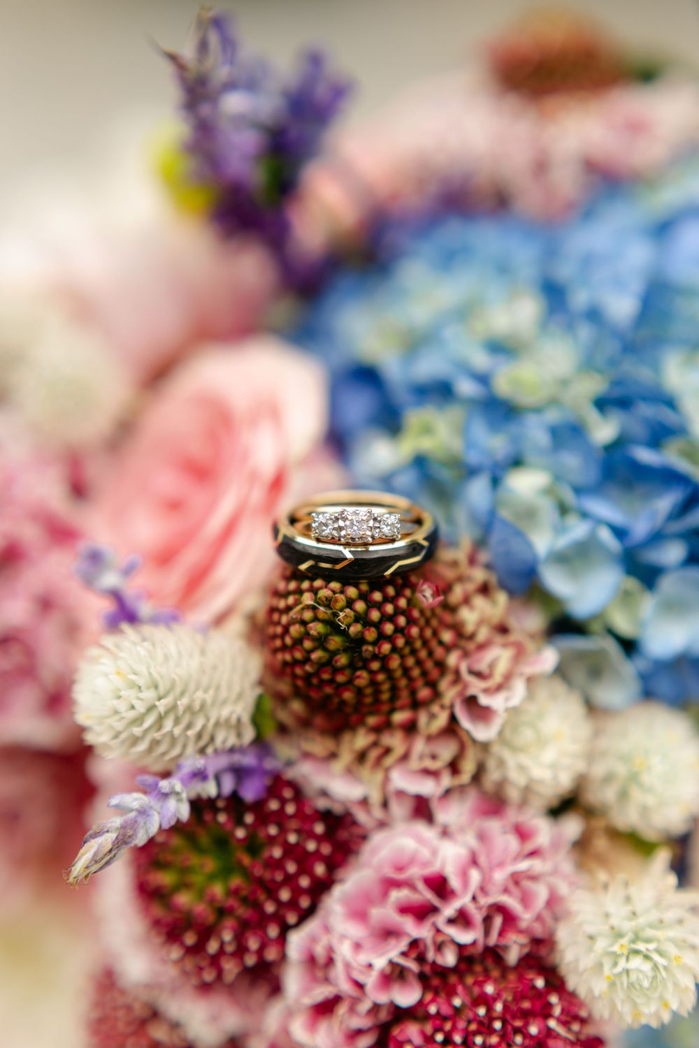 Wedding rings resting on a vibrant colorful bridal bouquet with hydrangeas, roses, and mixed blooms.