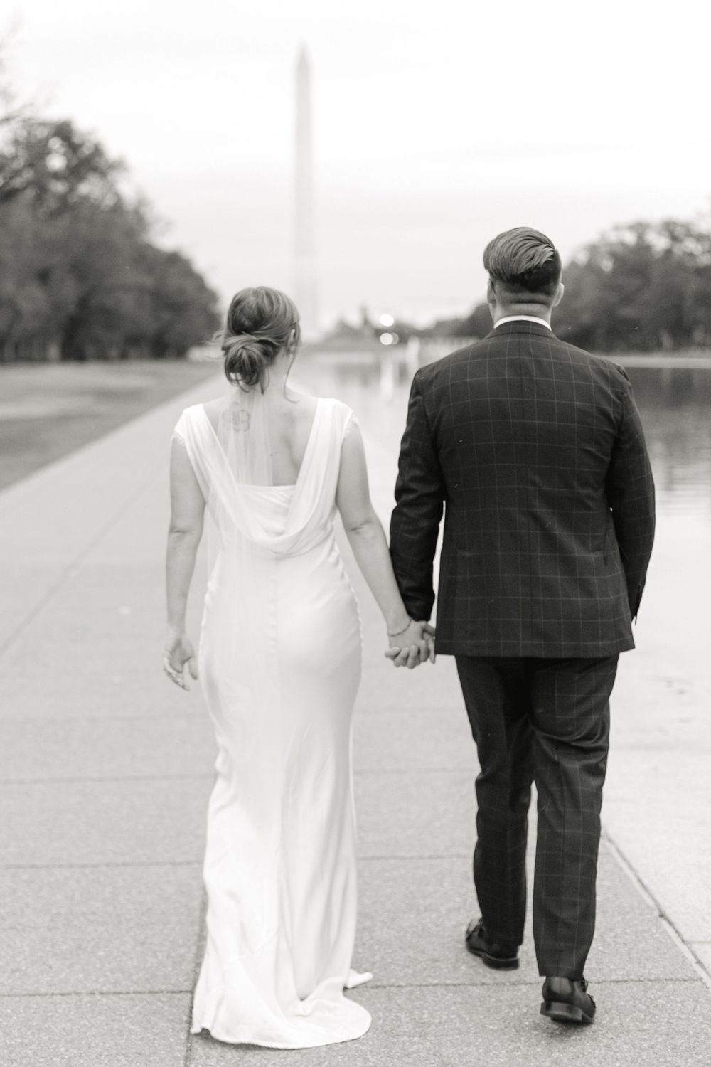 Black and white photo of bride and groom holding hands walking toward Washington Monument.