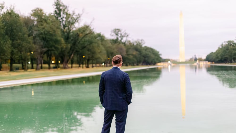 Groom in navy suit stands before the Reflecting Pool with Washington Monument in background.
