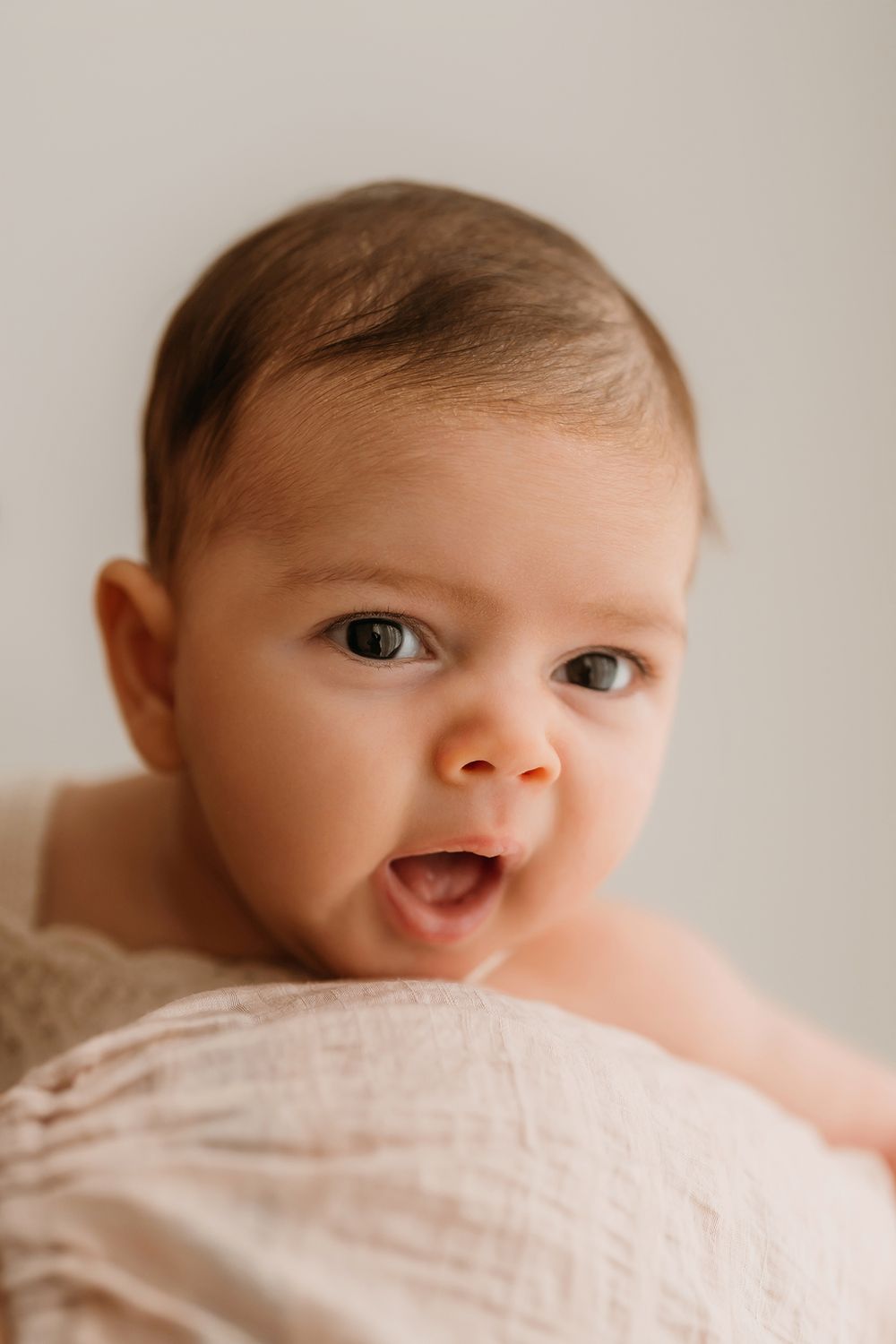 A series of close-up photos showing a baby's face peeking out from white blankets with different expressions.