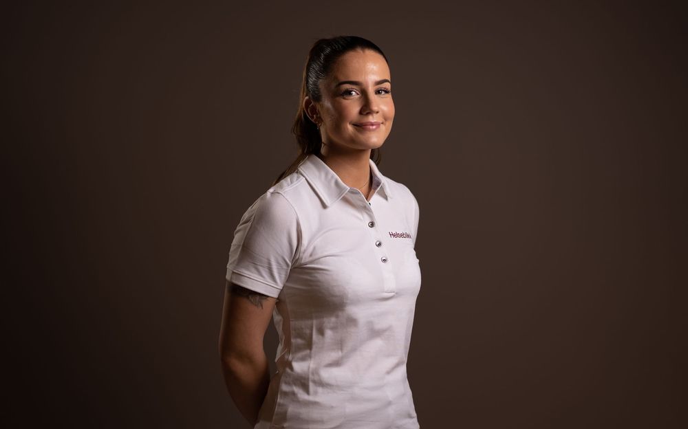 Person in white polo shirt against dark background in professional portrait setting.
