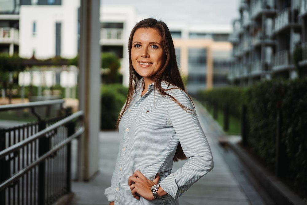Professional in light button-down shirt poses confidently on urban balcony.