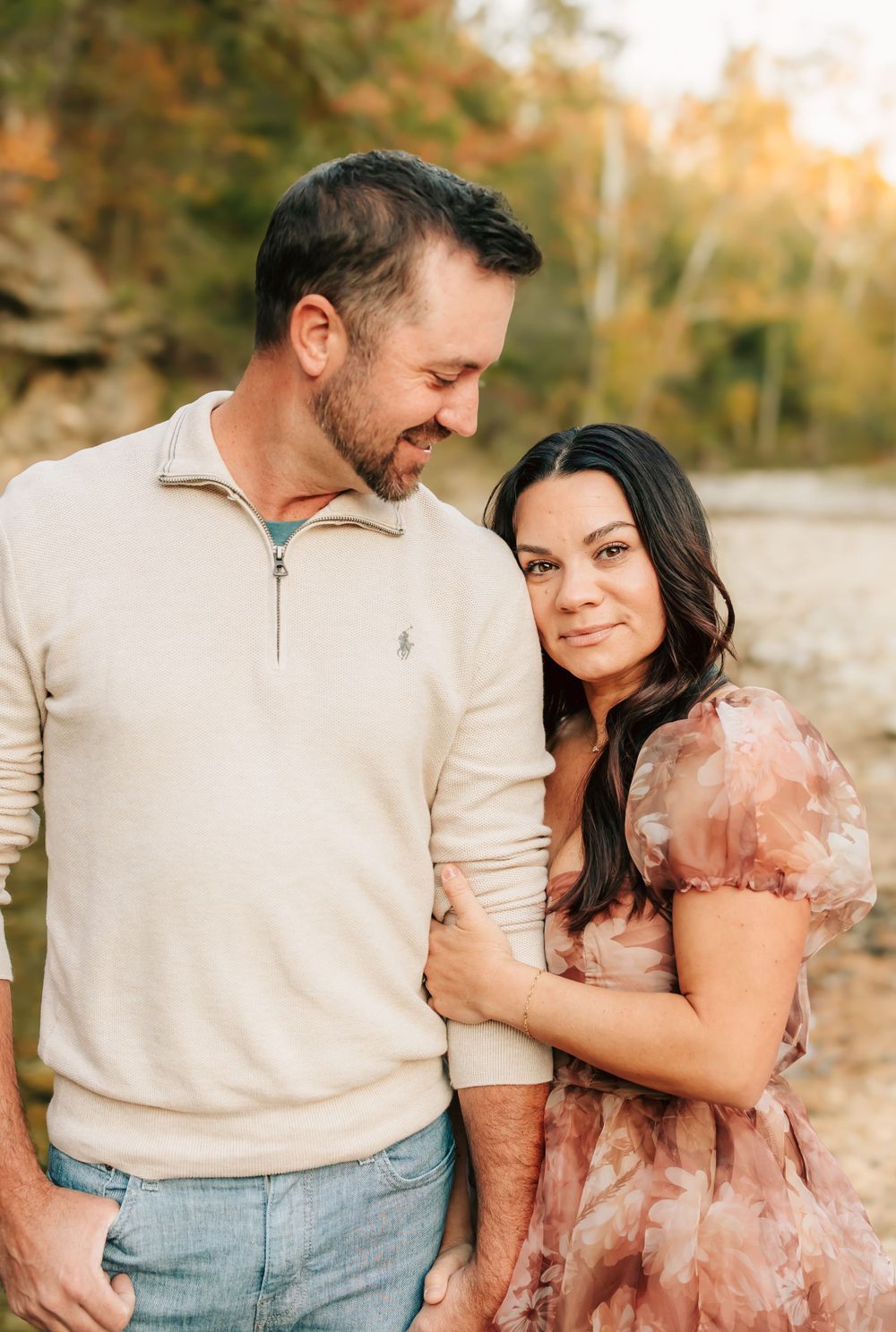 A couple shares a tender moment outdoors against an autumn backdrop wearing casual attire.
