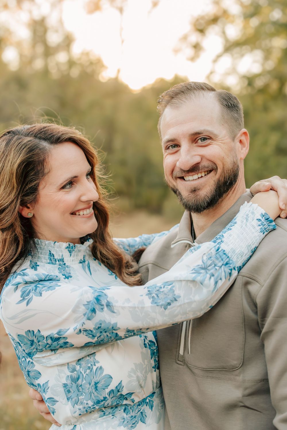 A couple shares a joyful moment outdoors wearing coordinated blue and gray outfits during golden hour.