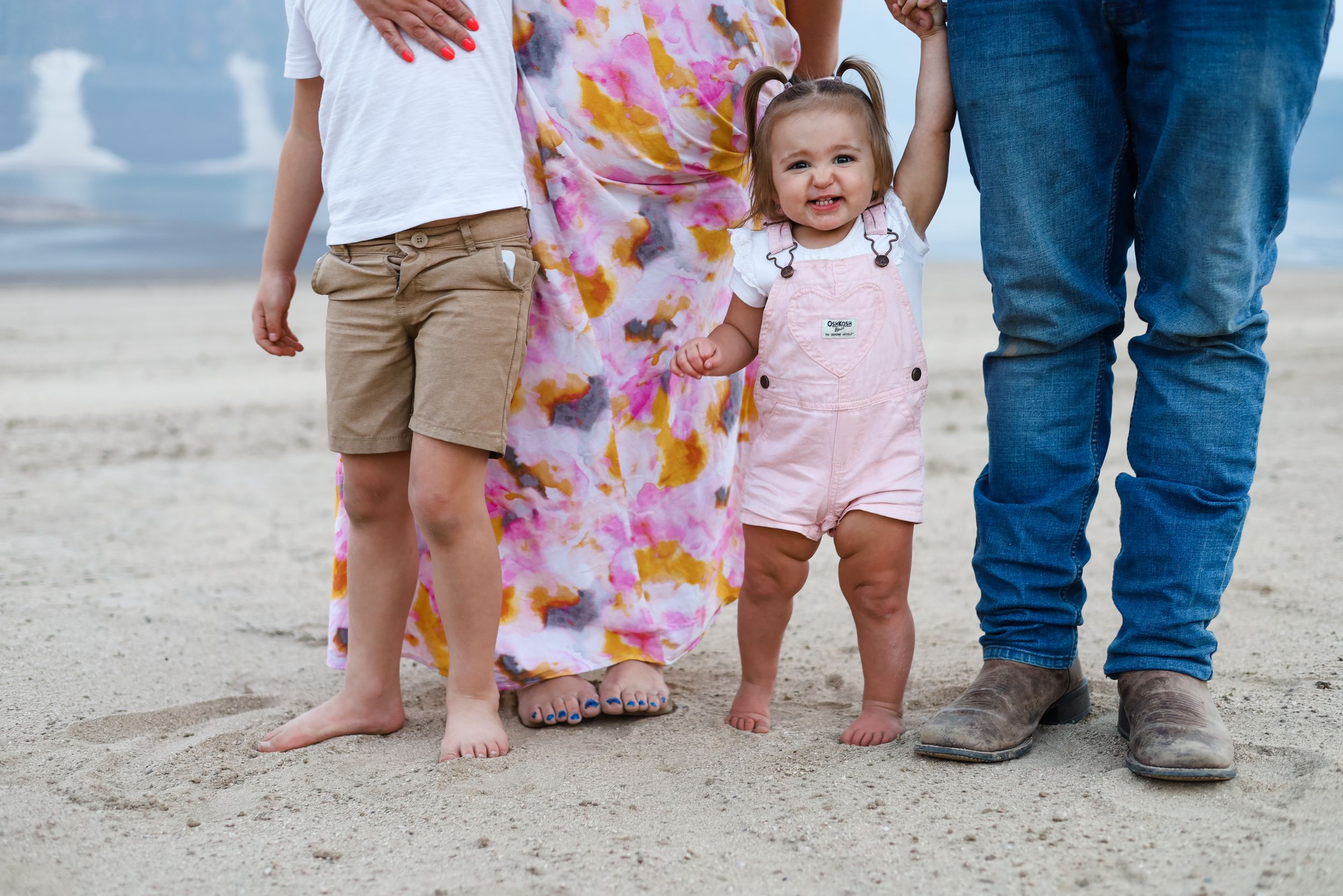 Small children walk along sandy beach wearing colorful summer outfits.