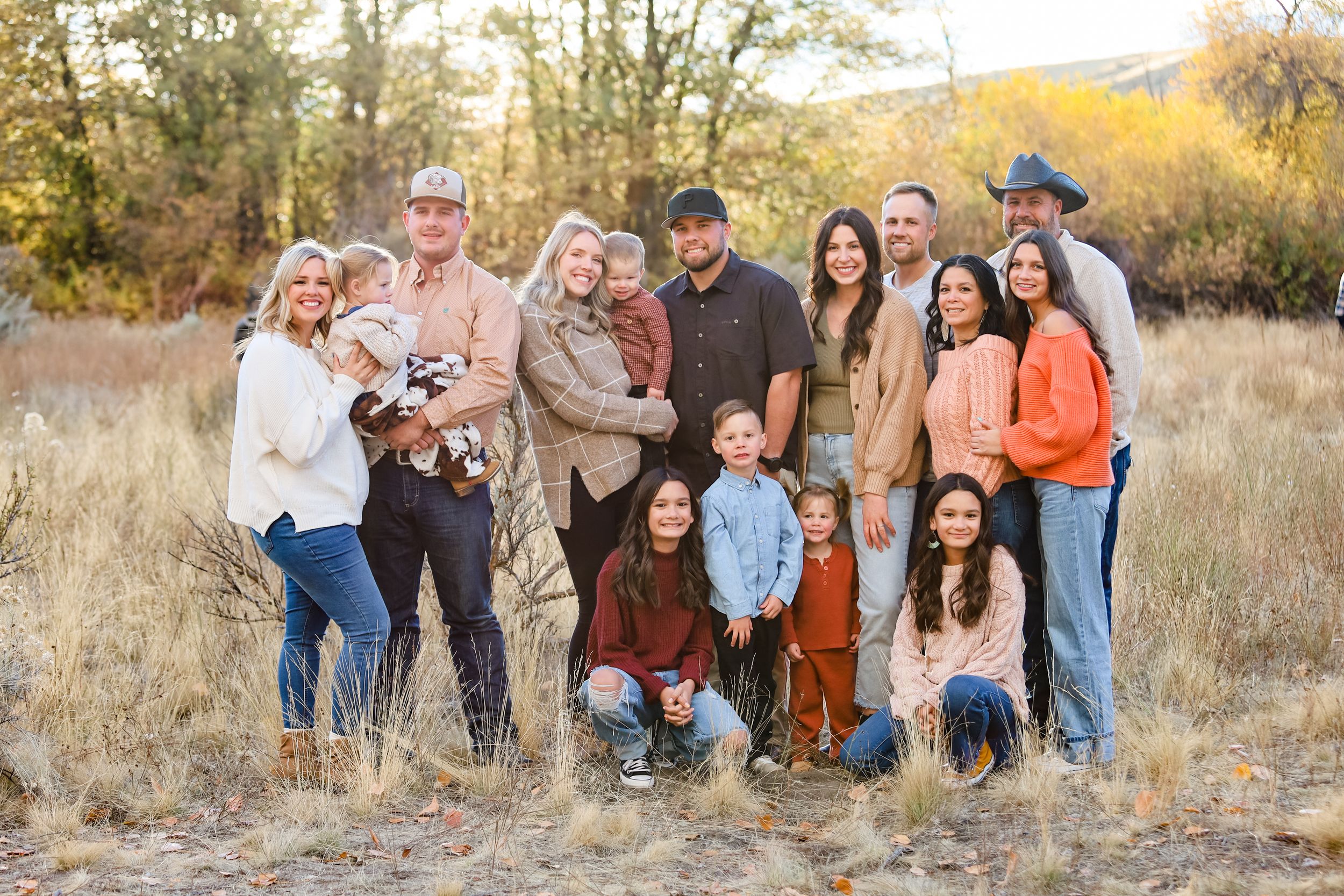 A group poses together in a golden field during sunset for outdoor family portraits.
