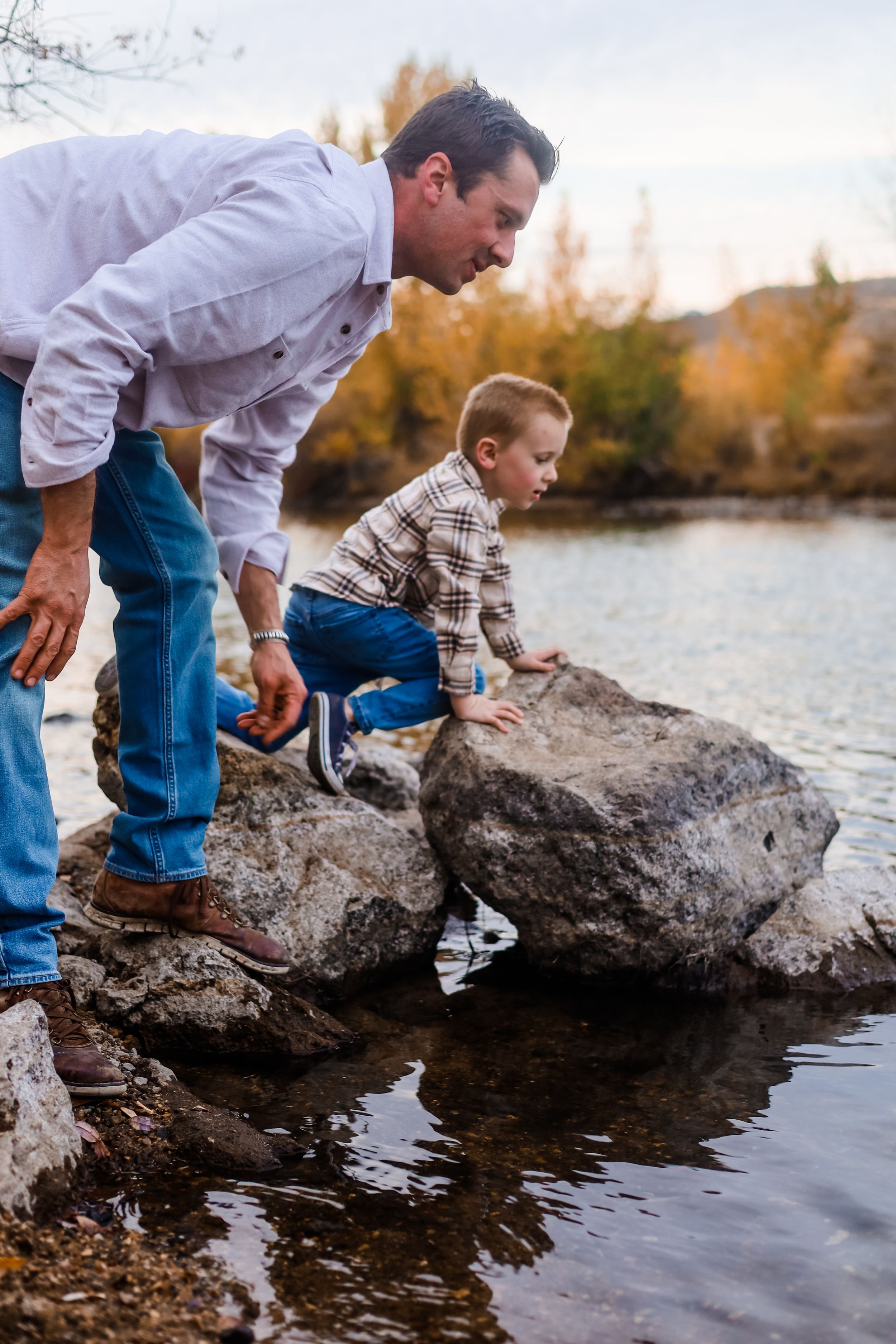 Parent and child exploring rocks by the water's edge.