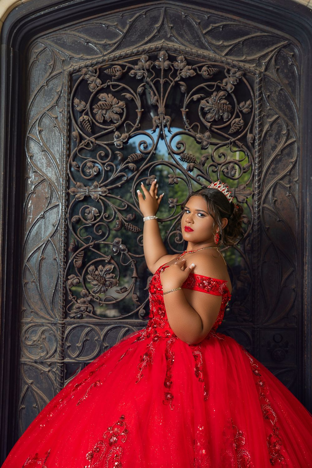 Red ballgown against ornate wrought iron backdrop with dramatic lighting.