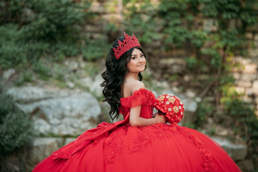 Flowing red princess gown with dramatic tulle skirt against stone wall backdrop.