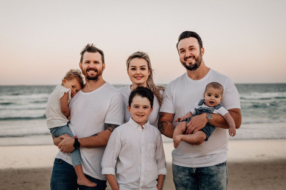 Family enjoying a tender moment together on the beach at sunset in casual white and denim outfits.