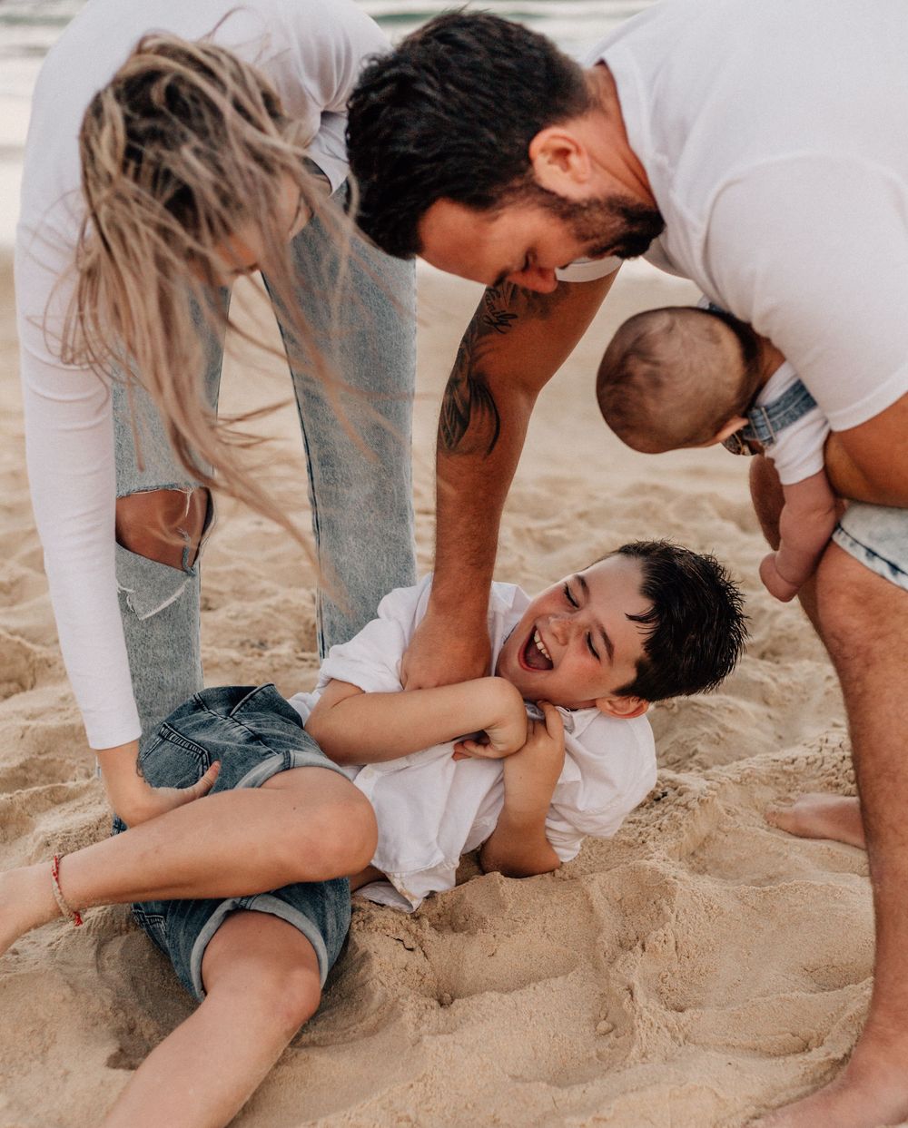 Candid sequence of family members playing and tickling on sandy beach during sunset photoshoot.