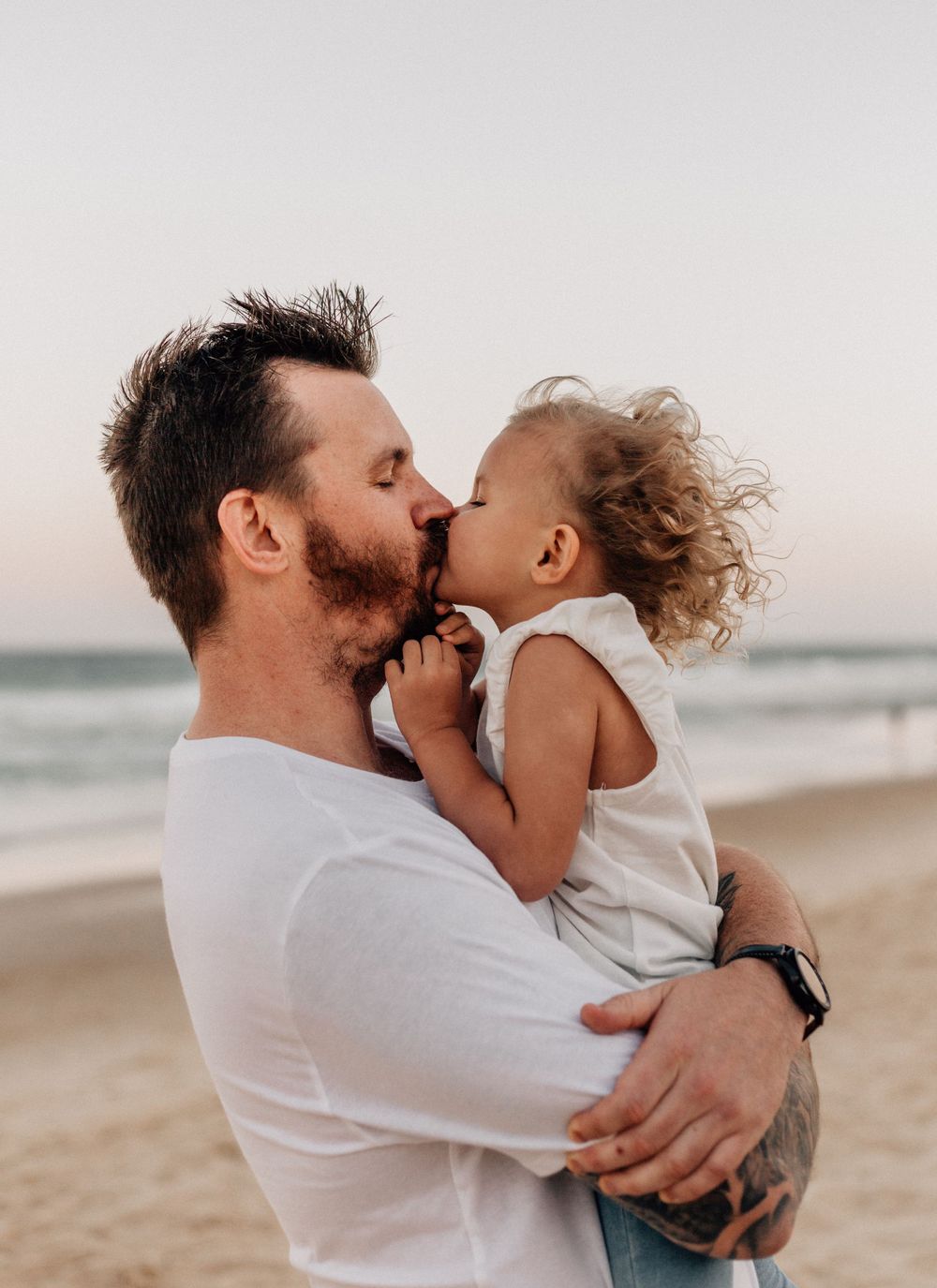 Sweet moments of affection captured during a beachside family photo session at dusk.