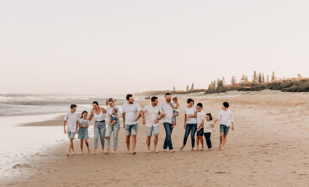 Extended family group walking along a peaceful beach shoreline at sunset.
