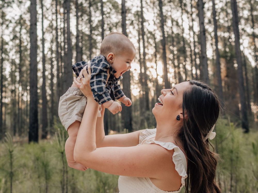 Joyful moment between parent and baby lifted in air among pine trees.