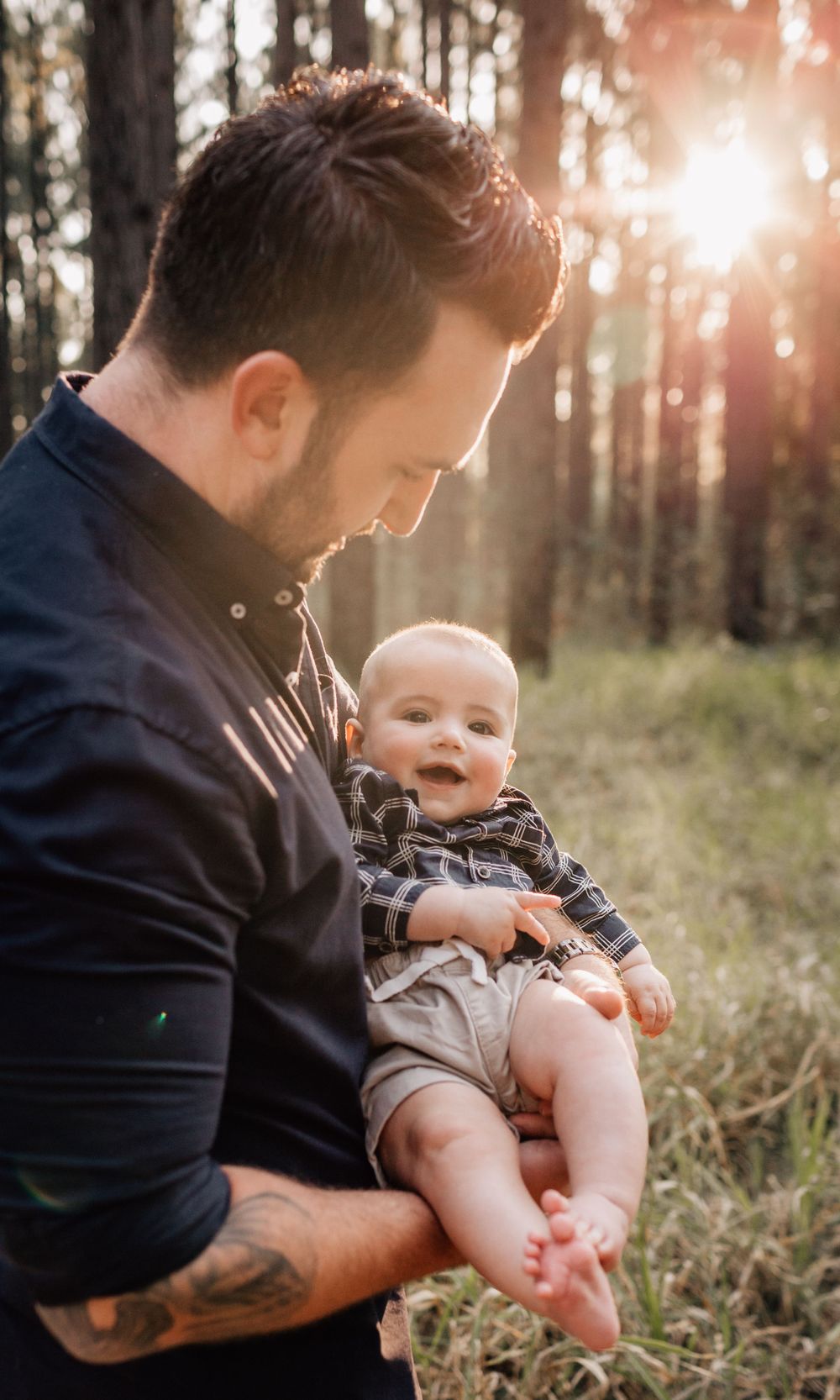 Parent holding baby in forest setting with sunlight streaming through trees.