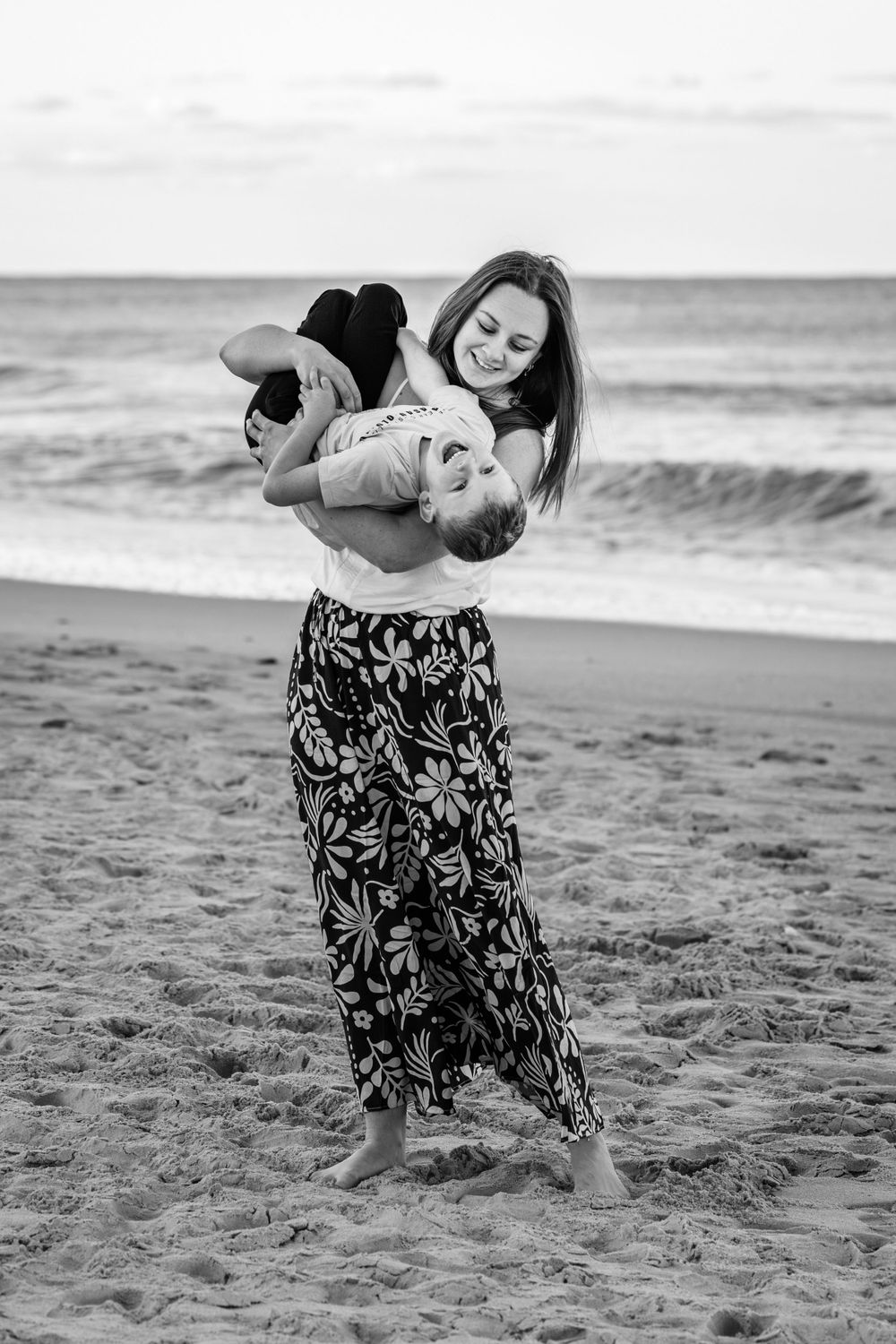 Black and white beach portrait series showing tender family moment on sandy shore.