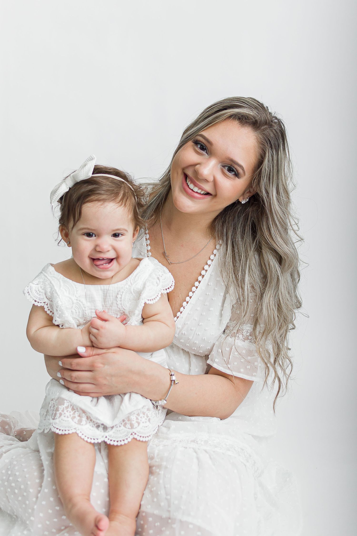 Bright and airy studio portrait of a smiling mother holding her joyful toddler, both dressed in white, captured by Lively Ella Photography.