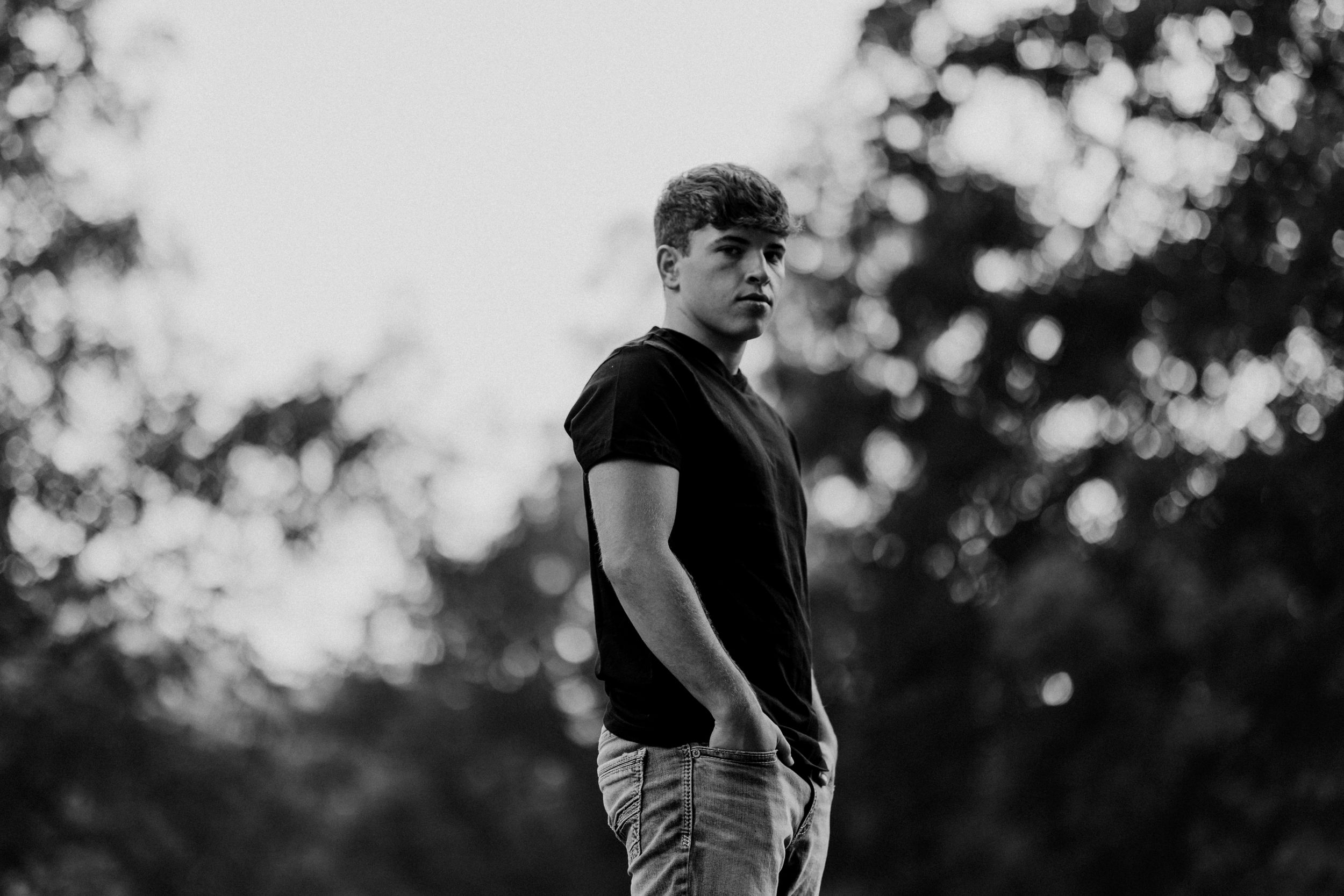 Person in black t-shirt stands in dramatic black and white portrait outdoors.