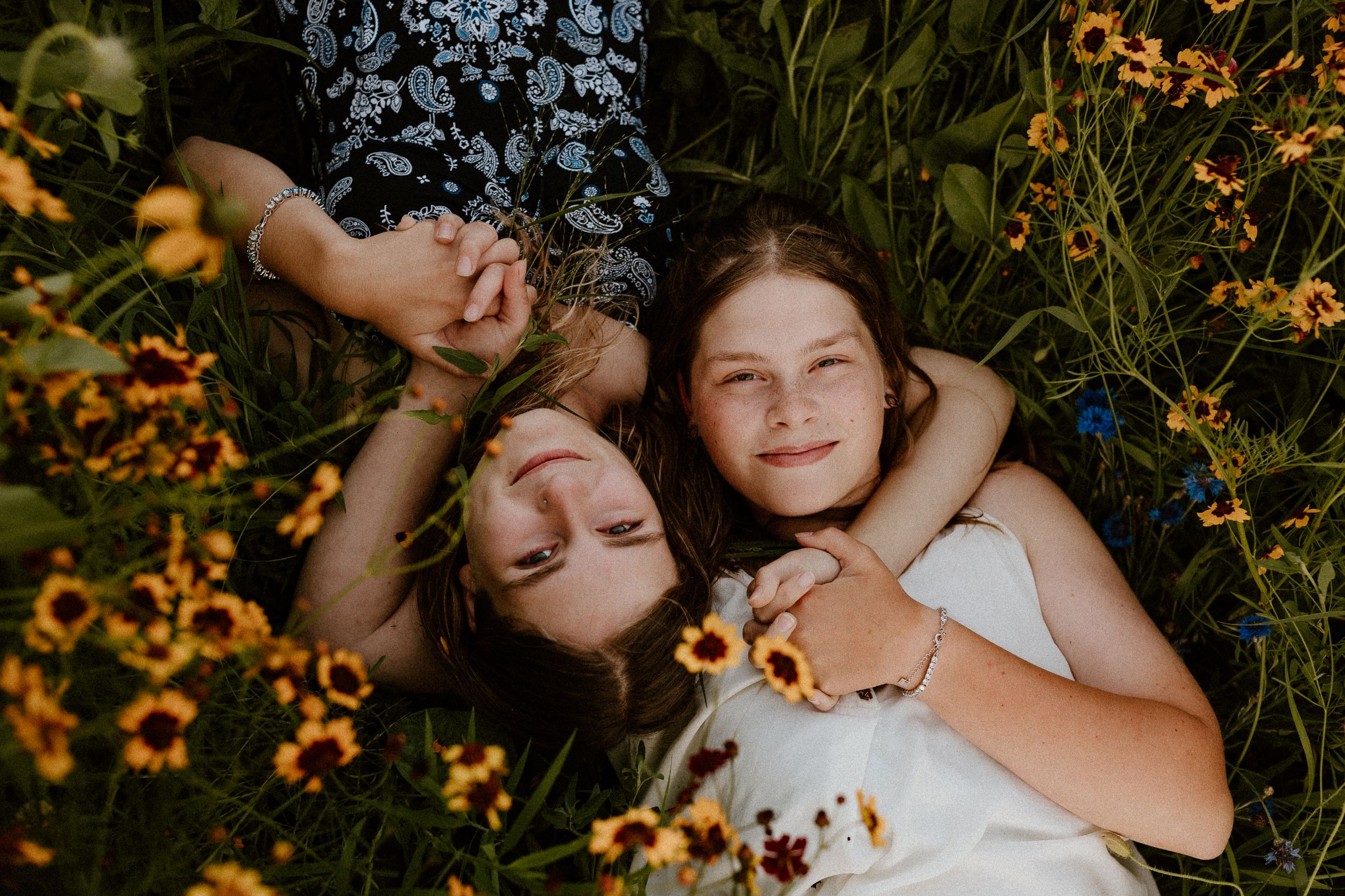 Two friends lying in wildflowers during golden hour photography.