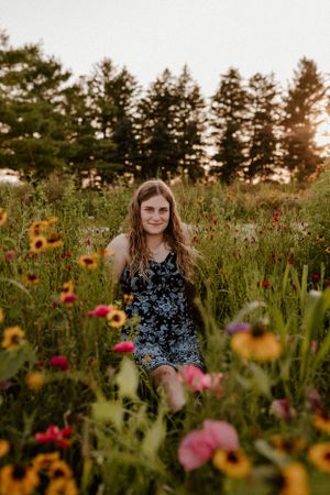 Person in floral dress sitting among colorful wildflowers during golden hour.
