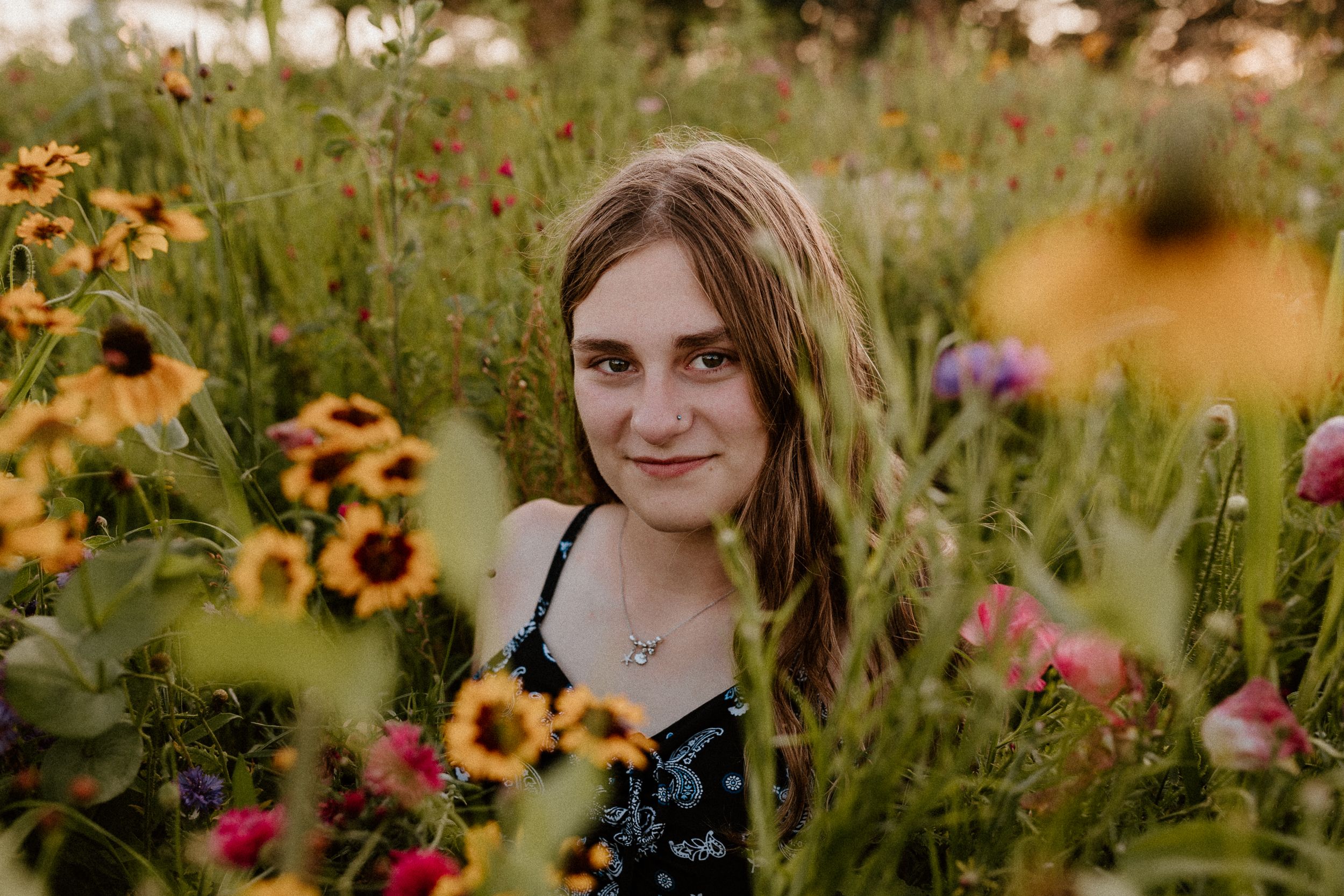 Person in floral dress surrounded by vibrant sunflowers and wildflowers in meadow.
