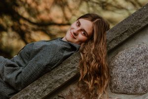 Artistic autumn portrait against a stone backdrop with warm lighting and bokeh effect.