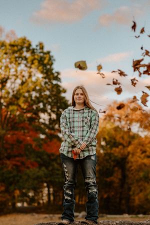 Autumn portrait with falling leaves and golden sunset lighting in a forest setting.